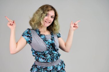 Güzel, muhteşem saçlı bir kız öğrencinin portresi. Turkuaz elbiseli genç bir kadının yatay fotoğrafı beyaz arka planda kameranın önünde duruyor..