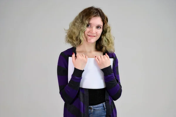 Concept horizontal photo of a young woman with emotions in a dark jacket standing in front of the camera on a white background. Portrait of a student girl with a folder in her hands with fluffy hair. — Stock Photo, Image