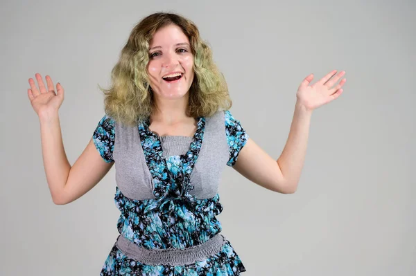 Concept horizontal photo of a young woman with emotions in a turquoise dress stands in front of the camera on a white background. Portrait of a student girl with beautiful magnificent hair.