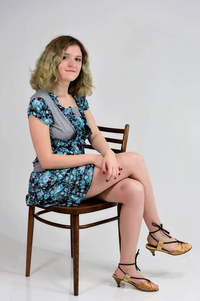 Concepto de foto vertical de una joven con un vestido de color turquesa sentada en una silla delante de la cámara sobre un fondo blanco. Retrato de una estudiante con hermoso cabello magnífico . — Foto de Stock