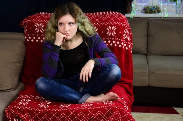 Das horizontale Konzeptfoto einer jungen Frau in Pullover und Jeans sitzt auf einem Stuhl vor der Kamera im Innenraum des Hauses. Porträt eines Mädchens mit wunderschönem prachtvollen Haar fehlt auf dem Sofa. — Stockfoto