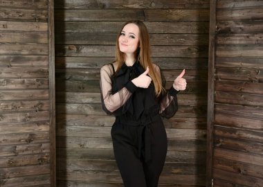 Ev konforu kavramı. Koyu renk elbiseli, güzel esmer bir kızın fotoğrafı. Evin içinde ahşap bir arka planda duruyor, gülümsüyor..