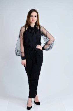 Güzel, gülümseyen bir kızın tam boy fotoğrafı koyu renk elbiseli esmer bir kız beyaz arka planda duruyor ve duygularıyla konuşuyor. Bir afiş için konsept portresi.