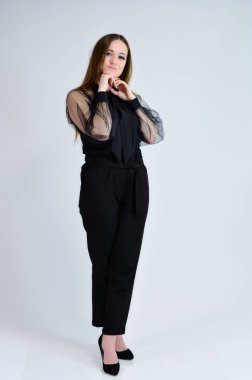 Güzel, gülümseyen bir kızın tam boy fotoğrafı koyu renk elbiseli esmer bir kız beyaz arka planda duruyor ve duygularıyla konuşuyor. Bir afiş için konsept portresi.