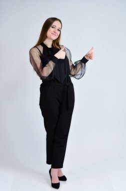 Güzel, gülümseyen bir kızın tam boy fotoğrafı koyu renk elbiseli esmer bir kız beyaz arka planda duruyor ve duygularıyla konuşuyor. Bir afiş için konsept portresi.