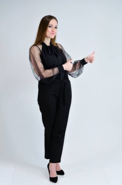 Güzel, gülümseyen bir kızın tam boy fotoğrafı koyu renk elbiseli esmer bir kız beyaz arka planda duruyor ve duygularıyla konuşuyor. Bir afiş için konsept portresi.