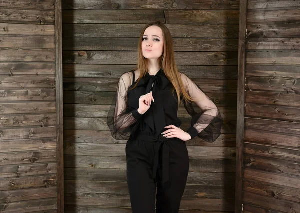 El concepto de confort en el hogar. Foto de una bonita chica morena con excelente maquillaje en ropa oscura de pie sobre un fondo de madera en el interior del hogar, sonriendo . —  Fotos de Stock