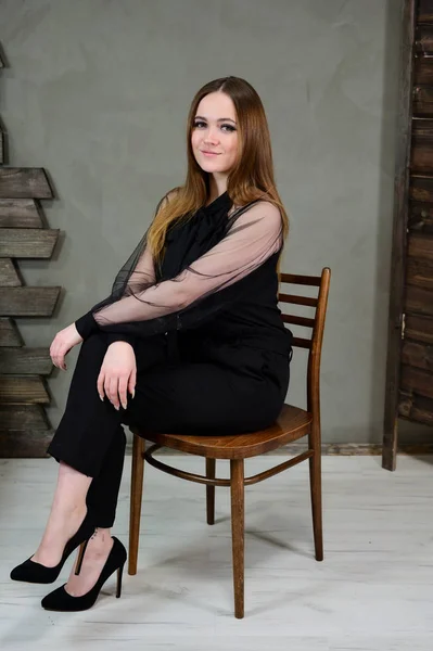 Full-length φωτογραφία ενός όμορφου μελαχρινού κοριτσιού με εξαιρετικό μακιγιάζ σε σκούρα ρούχα που κάθεται σε ένα περίπτερο σε γκρι φόντο σε ένα πολυτελές vintage εσωτερικό. Η έννοια της ένα λαμπερό πορτρέτο. — Φωτογραφία Αρχείου