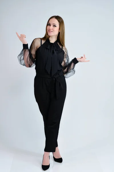 A full-length photo of a pretty smiling girl A brunette girl with excellent makeup in dark clothes is standing on a white background, talking with emotions. Concept portrait for a banner. — Stock Photo, Image