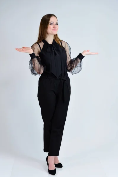 A full-length photo of a pretty smiling girl A brunette girl with excellent makeup in dark clothes is standing on a white background, talking with emotions. Concept portrait for a banner. — Stock Photo, Image