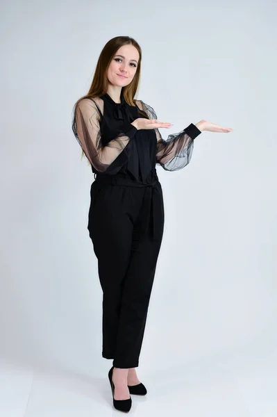 A full-length photo of a pretty smiling girl A brunette girl with excellent makeup in dark clothes is standing on a white background, talking with emotions. Concept portrait for a banner. — 스톡 사진