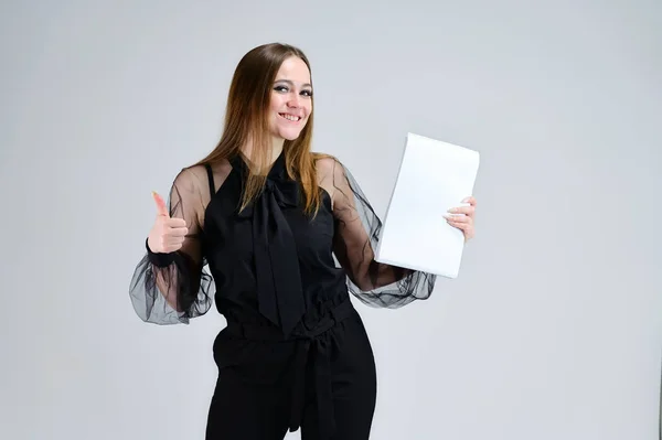 Retrato conceptual para una pancarta. Una foto de una chica morena bastante sonriente con una carpeta en sus manos con excelente maquillaje en ropa oscura está de pie sobre un fondo blanco . — Foto de Stock