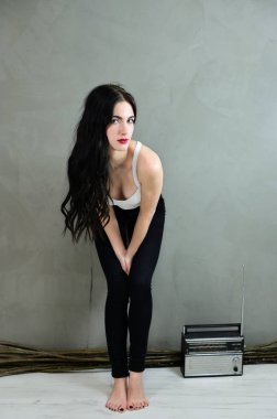 Göz alıcı bir kadın portresi konsepti. Uzun saçlı, güzel bir esmer kızın portresi. Kot pantolon ve gri arka planda tişörtü var. Gülümseyerek duvarın yanında duruyor..