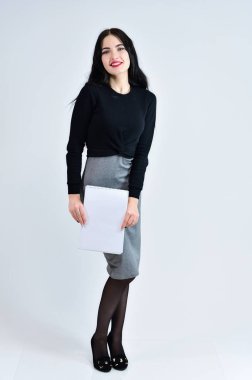 Esmer, uzun saçlı, güzel makyajlı, beyaz arka planda gri elbiseli, elinde klasörle duran bir kız. İş kadını portresi kavramı.