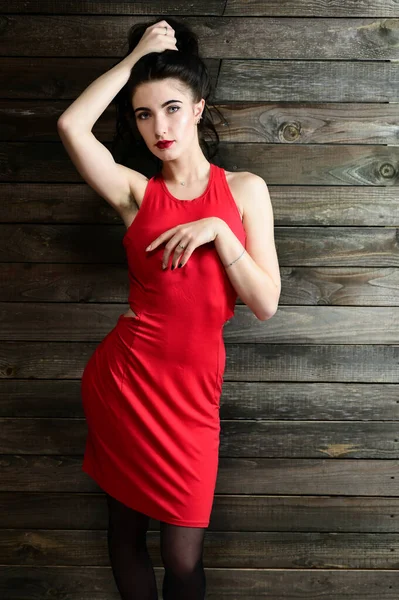 El concepto de un retrato femenino glamoroso. Retrato de una guapa morena con excelente maquillaje en un vestido rojo en un interior de madera delante de la cámara con una sonrisa . — Foto de Stock