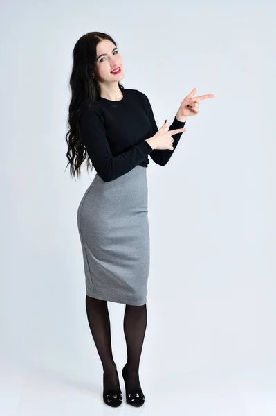 Retrato de una guapa morena con una sonrisa de pelo largo con excelente maquillaje en un vestido gris sobre un fondo blanco está de pie derecho. Concepto de retrato de mujer de negocios . — Foto de Stock