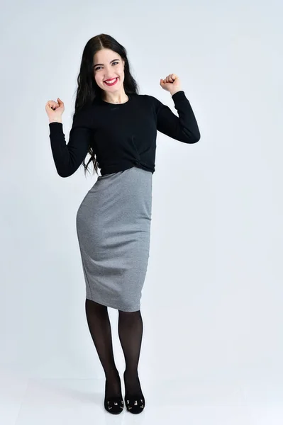 Concepto de retrato de mujer de negocios. Una chica morena con una sonrisa con el pelo largo con un maquillaje excelente en un vestido gris sobre un fondo blanco se encuentra justo en diferentes poses en pleno crecimiento . — Foto de Stock