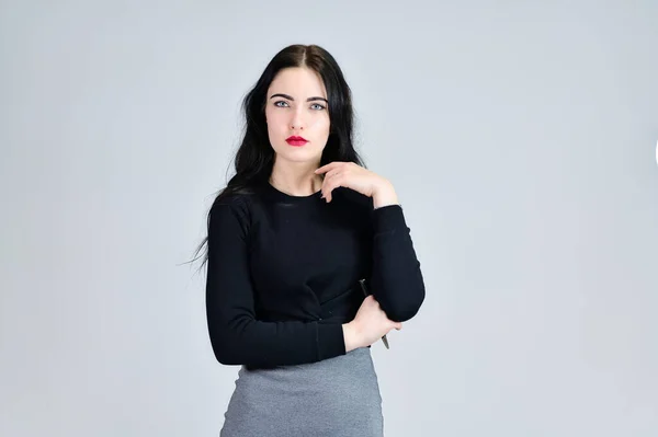 Retrato de una chica morena con una sonrisa de pelo largo con excelente maquillaje en un vestido gris sobre un fondo blanco en diferentes poses. Concepto de negocio foto retrato femenino con emociones . — Foto de Stock