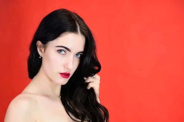 Het concept van een glamoureus vrouwenportret. Portret van een brunette meisje met een glimlach met lang haar met uitstekende make-up op een rode achtergrond in verschillende poses zijaanzicht. — Stockfoto