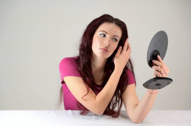 Model gülümser ve aynanın önünde makyaj yapar. Pembe elbiseli, kahverengi saçlı, ince, esmer bir kadının portresi stüdyoda beyaz bir arka planda bir masada oturuyor..