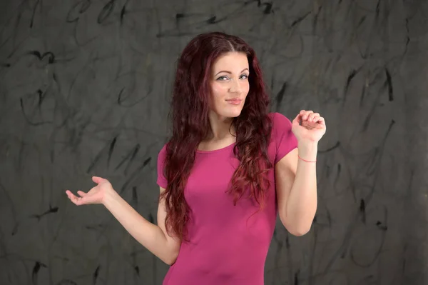 Modello glamour è sorridente e parlando carino alla fotocamera. Ritratto di una donna bruna piuttosto magra con emozioni in un vestito rosa e con i capelli castani su uno sfondo grigio in studio . — Foto Stock