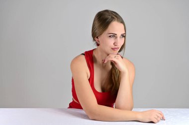 Beyaz arka planda evrensel bir kadın portresi. Stüdyodaki beyaz bir masada oturan uzun saçlı ve harika makyajlı güzel bir kızın yatay fotoğrafı..