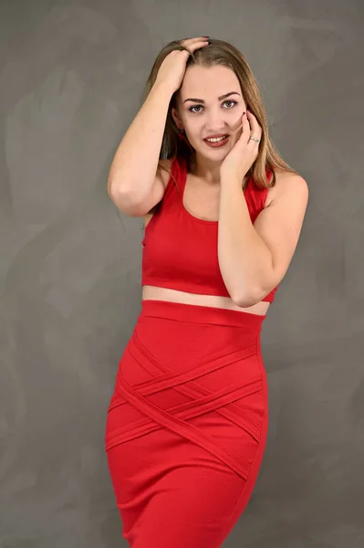 Verticale foto van een mooi lachend meisje met lang haar en geweldige make-up in een rode jurk met emoties in verschillende poses. Universeel concept van een vrouwelijk portret. — Stockfoto