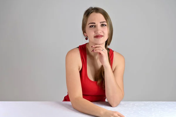 Universal concept female portrait on a white background. Horizontal photo of a pretty smiling girl with long hair and great makeup sitting at a white table in the studio. — Stock Photo, Image