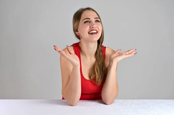 Retrato feminino conceito universal em um fundo branco. Foto horizontal de uma garota muito sorridente com cabelo comprido e ótima maquiagem sentada em uma mesa branca no estúdio . — Fotografia de Stock