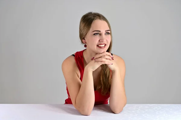 Concepto universal retrato femenino sobre fondo blanco. Foto horizontal de una chica muy sonriente con el pelo largo y un gran maquillaje sentado en una mesa blanca en el estudio . — Foto de Stock