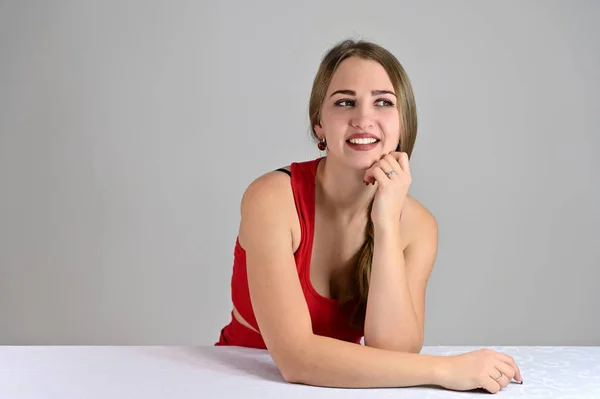 Concepto universal retrato femenino sobre fondo blanco. Foto horizontal de una chica muy sonriente con el pelo largo y un gran maquillaje sentado en una mesa blanca en el estudio . — Foto de Stock