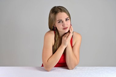 Stüdyodaki beyaz bir masada oturan uzun saçlı ve harika makyajlı güzel bir kızın yatay fotoğrafı. Beyaz arka planda evrensel konsept kadın portresi.