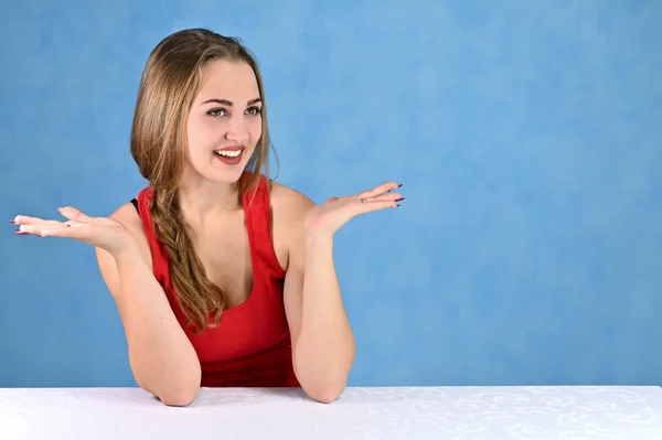 Universal concept female portrait on a blue background. Horizontal photo of a pretty smiling girl with long hair and great makeup sitting at a white table in the studio. — 스톡 사진