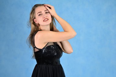 Siyah elbiseli, uzun saçlı ve mükemmel makyajlı güzel bir kızın fotoğrafı farklı pozlarda duruyor. Mavi arka planda bir kadının evrensel konsept yatay portresi.