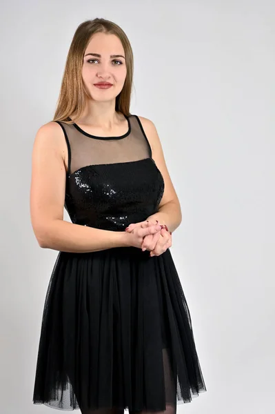 Ein Foto eines hübschen lächelnden Mädchens mit langen Haaren und exzellentem Make-up in einem schwarzen Kleid steht in verschiedenen Posen im Studio. universelles Konzept vertikales Frauenporträt auf weißem Hintergrund. — Stockfoto