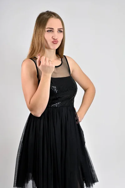 Μια φωτογραφία ενός όμορφου χαμογελαστού κοριτσιού με μακριά μαλλιά και εξαιρετικό μακιγιάζ με μαύρο φόρεμα στέκεται σε διάφορες πόζες στο στούντιο. Καθολική έννοια κάθετη γυναίκα πορτρέτο σε λευκό φόντο. — Φωτογραφία Αρχείου