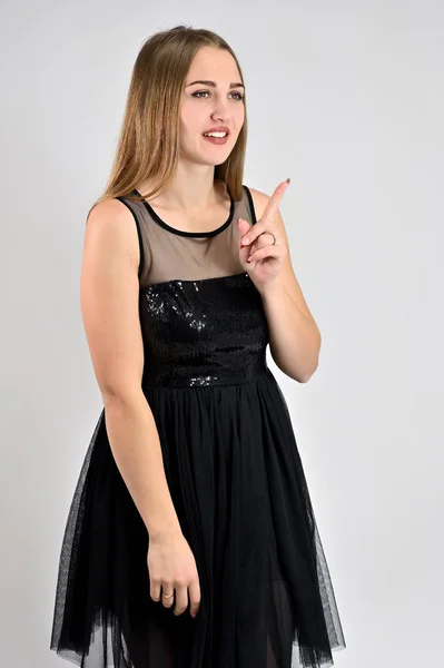 Ein Foto eines hübschen lächelnden Mädchens mit langen Haaren und exzellentem Make-up in einem schwarzen Kleid steht in verschiedenen Posen im Studio. universelles Konzept vertikales Frauenporträt auf weißem Hintergrund. — Stockfoto