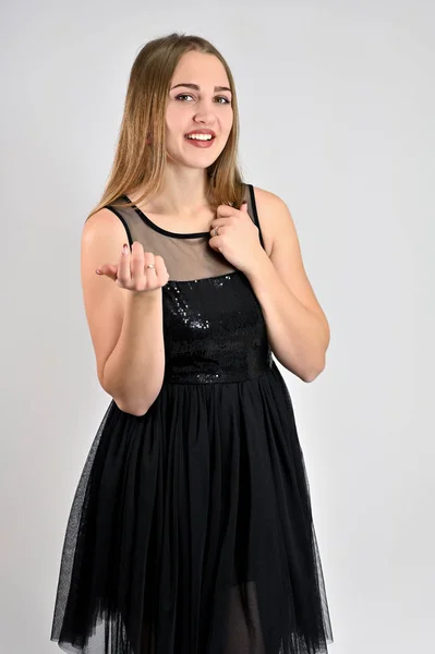 Une photo d'une jolie fille souriante avec les cheveux longs et un excellent maquillage dans une robe noire est debout dans diverses poses dans le studio. Concept universel portrait vertical de femme sur fond blanc . — Photo