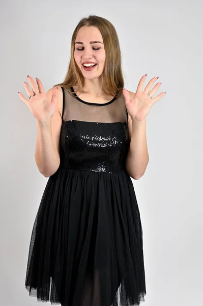 Concepto universal vertical retrato de mujer sobre fondo blanco. Una foto de una chica muy sonriente con el pelo largo y excelente maquillaje en un vestido negro está de pie en varias poses en el estudio . — Foto de Stock