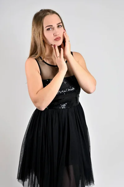 Universeel concept verticaal vrouwenportret op een witte achtergrond. Een foto van een vrij lachend meisje met lang haar en uitstekende make-up in een zwarte jurk staat in verschillende poses in de studio. — Stockfoto