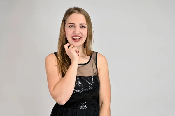 Retrato horizontal conceito universal de uma mulher sobre um fundo branco. Uma foto de uma menina muito sorridente com cabelo comprido e excelente maquiagem em um vestido preto fica em poses diferentes . — Fotografia de Stock