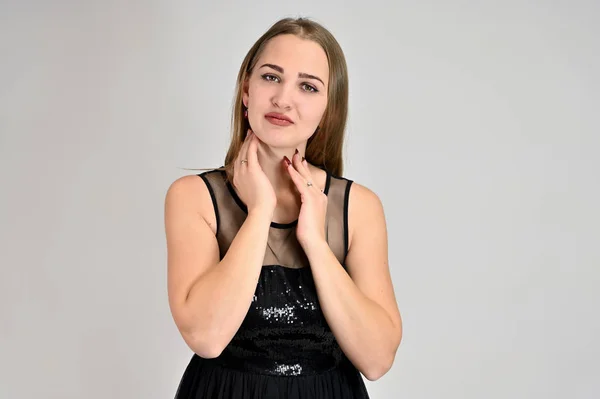 Concepto universal retrato horizontal de una mujer sobre un fondo blanco. Una foto de una chica muy sonriente con el pelo largo y excelente maquillaje en un vestido negro se para en diferentes poses . — Foto de Stock