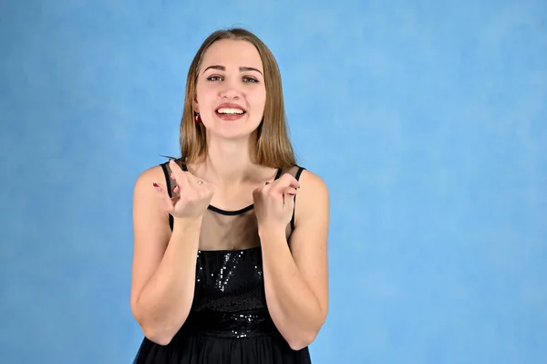 Universeel concept horizontaal portret van een vrouw op een blauwe achtergrond. Een foto van een mooi lachend meisje met lang haar en uitstekende make-up in een zwarte jurk staat in verschillende poses. — Stockfoto