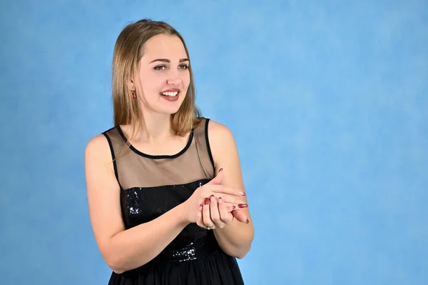 Concepto universal retrato horizontal de una mujer sobre un fondo azul. Una foto de una chica muy sonriente con el pelo largo y excelente maquillaje en un vestido negro se para en diferentes poses . —  Fotos de Stock