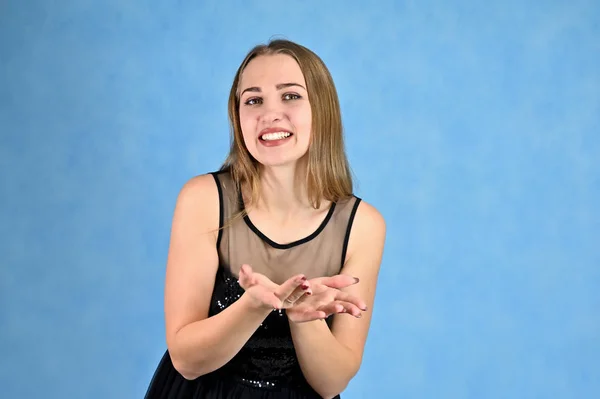 Concepto universal retrato horizontal de una mujer sobre un fondo azul. Una foto de una chica muy sonriente con el pelo largo y excelente maquillaje en un vestido negro se para en diferentes poses . —  Fotos de Stock