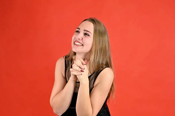 Una foto de una chica muy sonriente con el pelo largo y excelente maquillaje en un vestido negro se encuentra en diferentes poses. Concepto universal retrato femenino horizontal sobre fondo rojo . —  Fotos de Stock