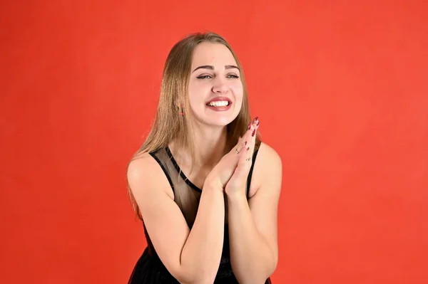 Universal concept horizontal female portrait on a red background. A photo of a pretty smiling girl with long hair and excellent make-up in a black dress stands in different poses. — 스톡 사진