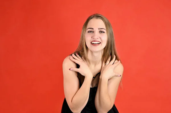 Retrato feminino horizontal conceito universal sobre um fundo vermelho. Uma foto de uma menina muito sorridente com cabelo comprido e excelente maquiagem em um vestido preto fica em poses diferentes . — Fotografia de Stock