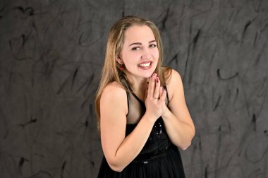 Siyah elbiseli, uzun saçlı ve mükemmel makyajlı güzel bir kızın fotoğrafı farklı pozlarda duruyor. Gri arka planda yatay kadın portresi evrensel kavramı.