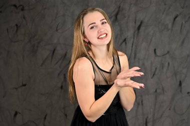 Siyah elbiseli, uzun saçlı ve mükemmel makyajlı güzel bir kızın fotoğrafı farklı pozlarda duruyor. Gri arka planda yatay kadın portresi evrensel kavramı.